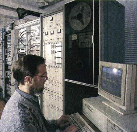 An observer in the VLBI room. The tape deck in the background is recording the radio signals for future analysis.